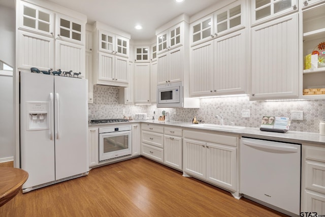 kitchen with stainless steel appliances, white cabinetry, backsplash, sink, and light hardwood / wood-style floors