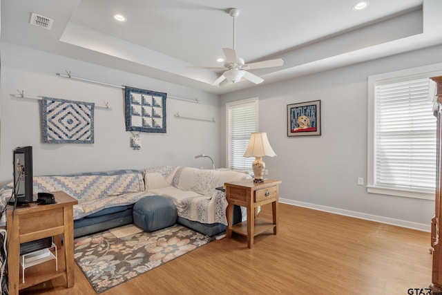 living room with light hardwood / wood-style flooring, ceiling fan, and a tray ceiling