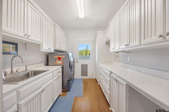 clothes washing area with light hardwood / wood-style floors, washer / clothes dryer, cabinets, and sink