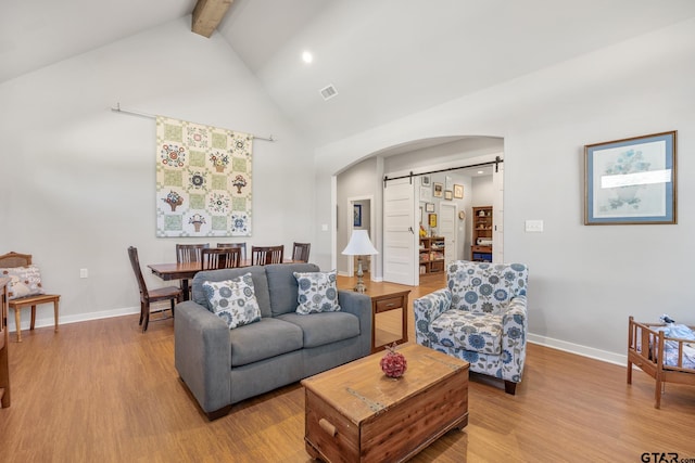 living room featuring a barn door, vaulted ceiling with beams, and light hardwood / wood-style flooring