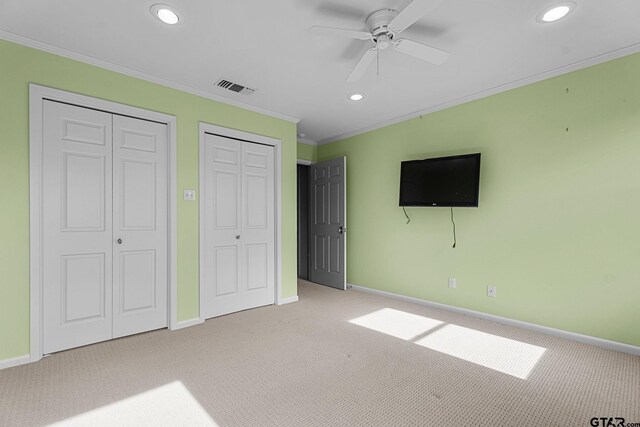 unfurnished bedroom with light carpet, crown molding, ceiling fan, and two closets