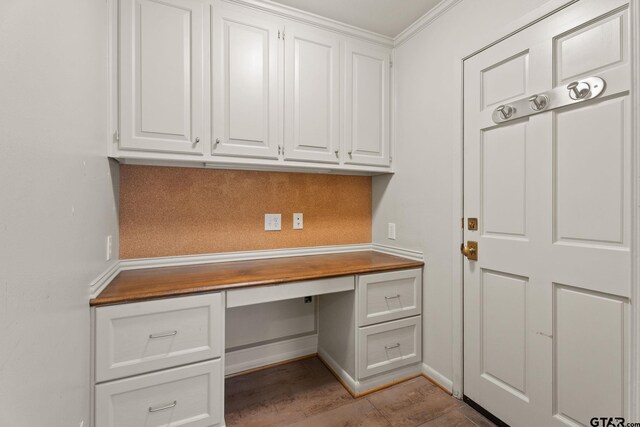 unfurnished office featuring light tile patterned flooring, built in desk, and crown molding