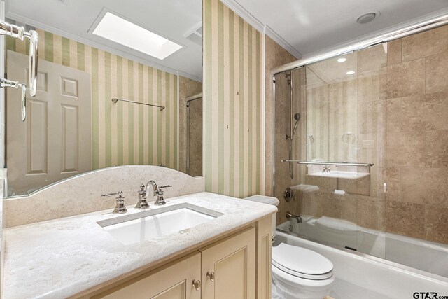 full bathroom featuring a skylight, ornamental molding, vanity, enclosed tub / shower combo, and toilet