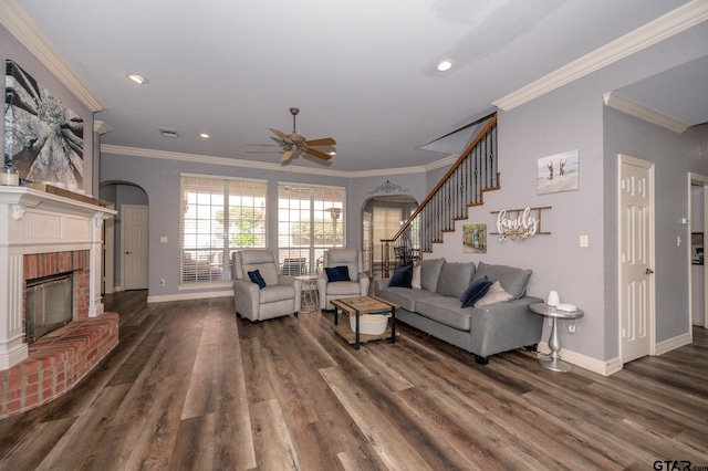 living room with dark wood-type flooring, ceiling fan, ornamental molding, and a brick fireplace