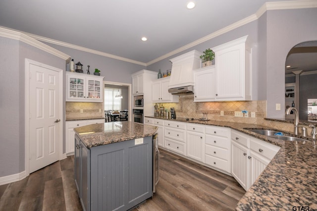 kitchen with white cabinetry, a kitchen island, sink, and dark stone countertops