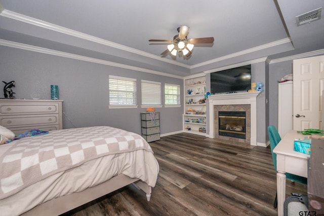 bedroom featuring crown molding, dark wood-type flooring, ceiling fan, a tiled fireplace, and a raised ceiling