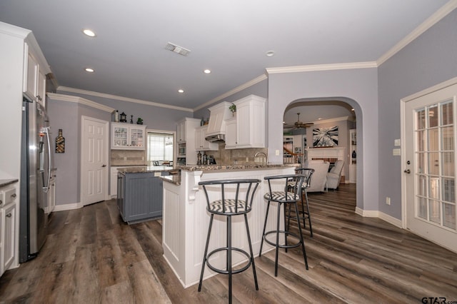 kitchen featuring a kitchen bar, white cabinetry, stainless steel fridge, kitchen peninsula, and stone counters