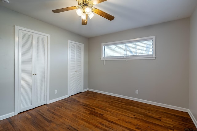 unfurnished bedroom featuring ceiling fan, dark hardwood / wood-style floors, and two closets