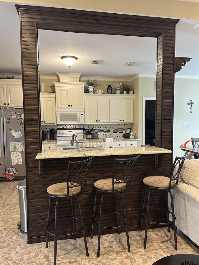 kitchen with white appliances, ornamental molding, a kitchen breakfast bar, and light stone countertops