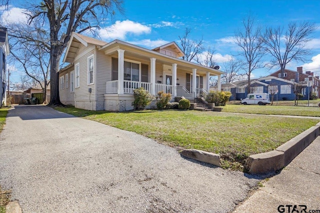 view of front of house featuring driveway, covered porch, a residential view, and a front yard