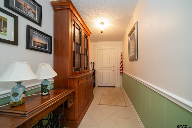 corridor featuring wainscoting, a textured ceiling, and light tile patterned floors