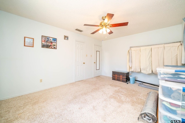 unfurnished bedroom featuring a textured ceiling, carpet, visible vents, and a ceiling fan