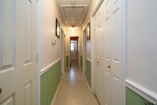 corridor with attic access, wainscoting, and light tile patterned flooring