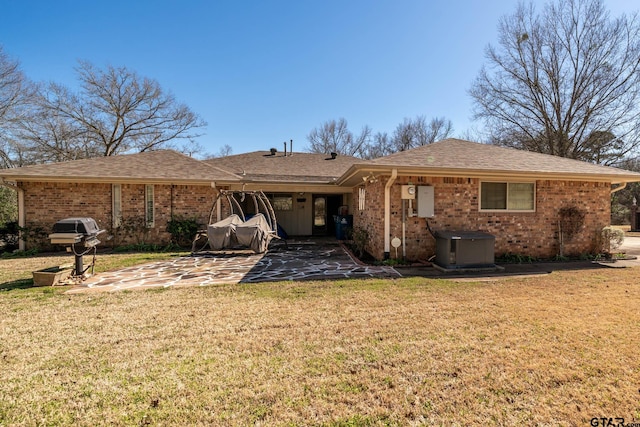 back of house with brick siding, a lawn, a patio area, and a shingled roof