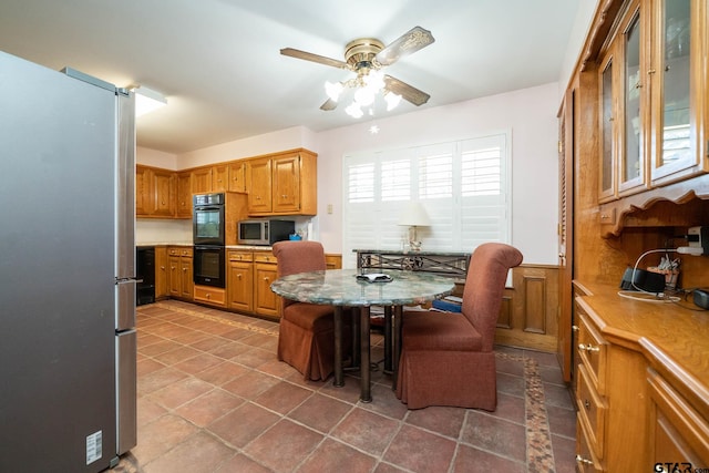 kitchen with ceiling fan, glass insert cabinets, appliances with stainless steel finishes, brown cabinets, and a kitchen bar