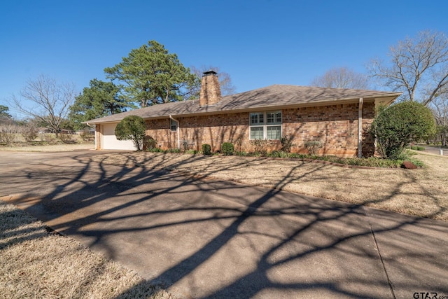 back of property with brick siding, a chimney, a shingled roof, a garage, and driveway