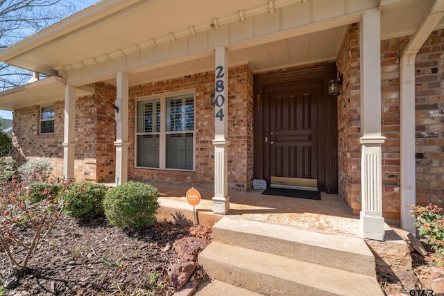 view of exterior entry with covered porch and brick siding