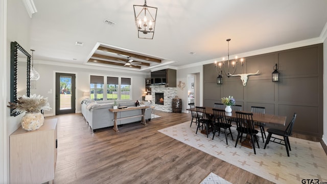 dining area featuring a raised ceiling, a stone fireplace, wood finished floors, visible vents, and ornamental molding
