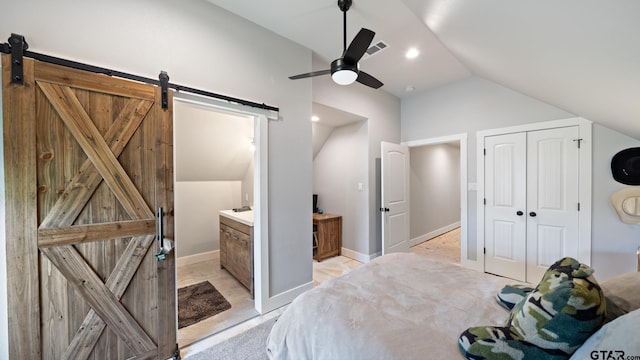 bedroom featuring ceiling fan, vaulted ceiling, ensuite bath, and a barn door