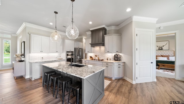 kitchen with crown molding, premium range hood, stainless steel appliances, and a center island with sink