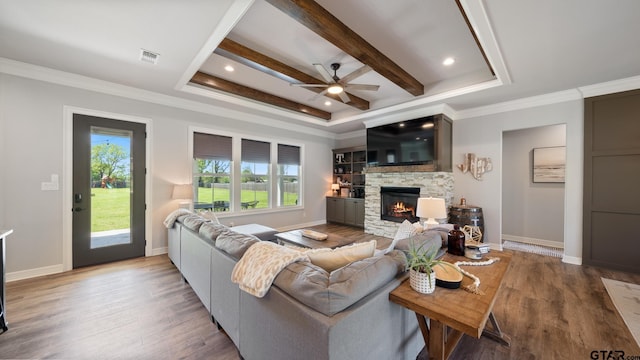 living area with a stone fireplace, ceiling fan, wood finished floors, and a healthy amount of sunlight