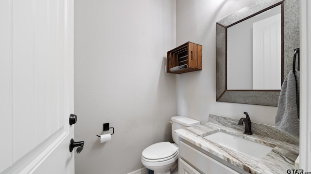 half bathroom with vanity, baseboards, and toilet