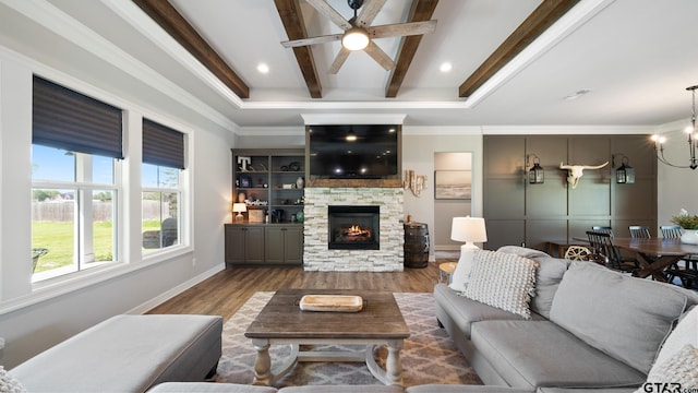 living area featuring a fireplace, ceiling fan with notable chandelier, baseboards, wood finished floors, and beamed ceiling
