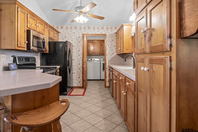 kitchen featuring stainless steel appliances, light tile patterned floors, vaulted ceiling, and washing machine and clothes dryer