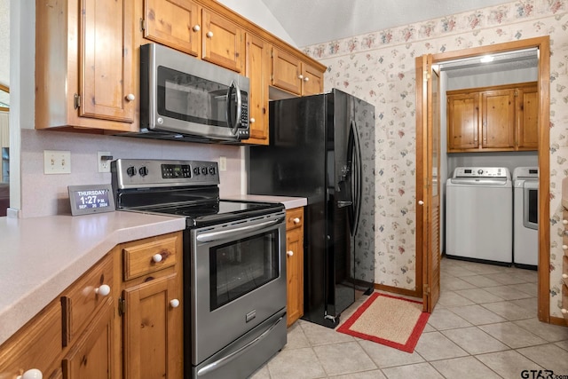 kitchen with lofted ceiling, appliances with stainless steel finishes, washing machine and clothes dryer, and light tile patterned floors