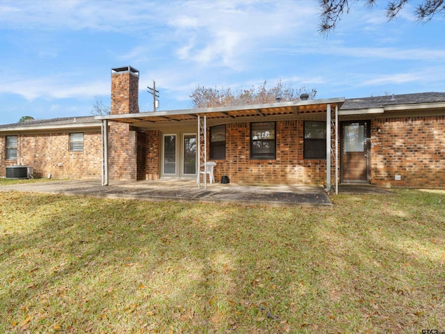 back of house featuring central AC unit, a patio, a chimney, a yard, and brick siding