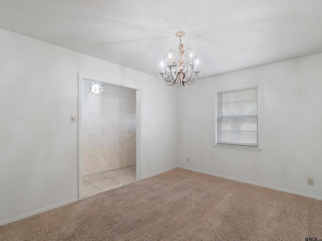 carpeted empty room featuring a textured ceiling, baseboards, tile patterned flooring, and a notable chandelier