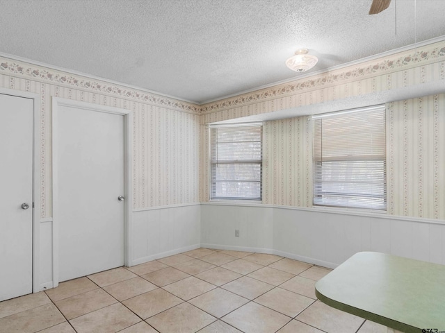 tiled spare room featuring wallpapered walls, a textured ceiling, and wainscoting