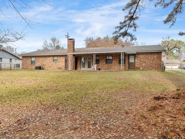 rear view of property featuring cooling unit, brick siding, fence, a yard, and a chimney