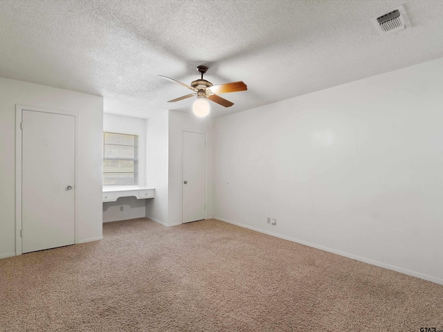 unfurnished bedroom with baseboards, visible vents, built in study area, ceiling fan, and carpet flooring