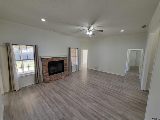 unfurnished living room with a fireplace, wood finished floors, visible vents, and a ceiling fan