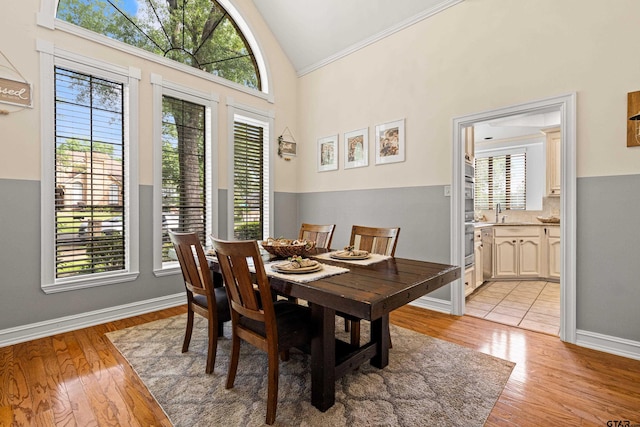 dining room featuring crown molding, baseboards, light wood-style flooring, and high vaulted ceiling