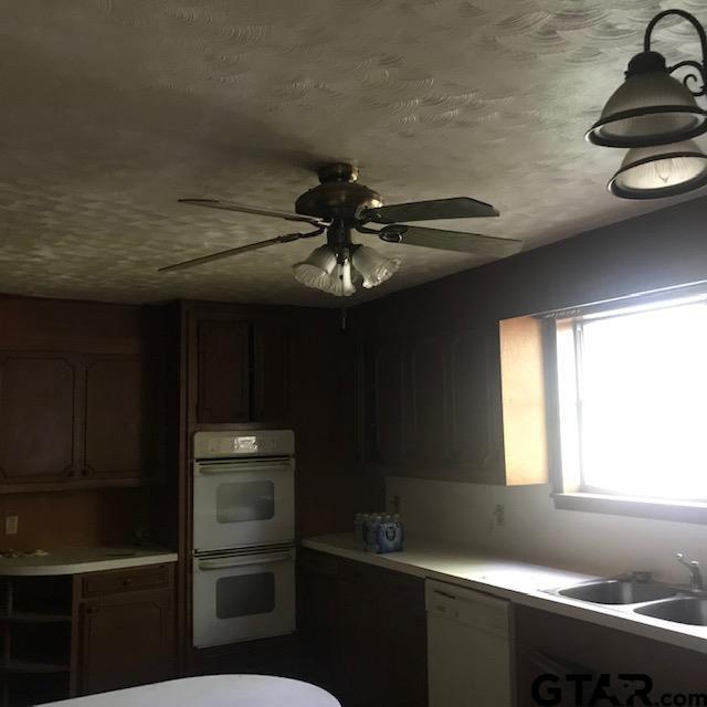 kitchen with a textured ceiling, sink, white appliances, and ceiling fan