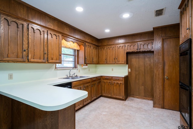 kitchen featuring a sink, brown cabinetry, visible vents, a peninsula, and light countertops