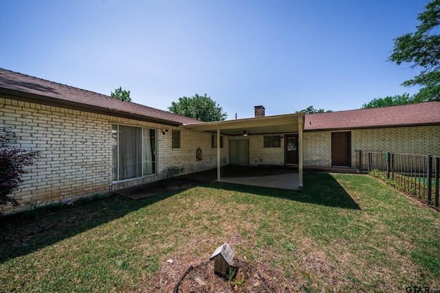 rear view of property with a patio, a chimney, a lawn, brick siding, and fence