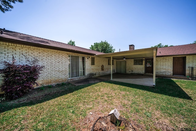 back of house featuring a lawn, brick siding, a patio, and a chimney
