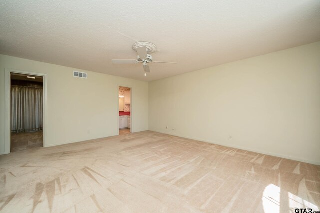 empty room featuring visible vents, light carpet, and a ceiling fan