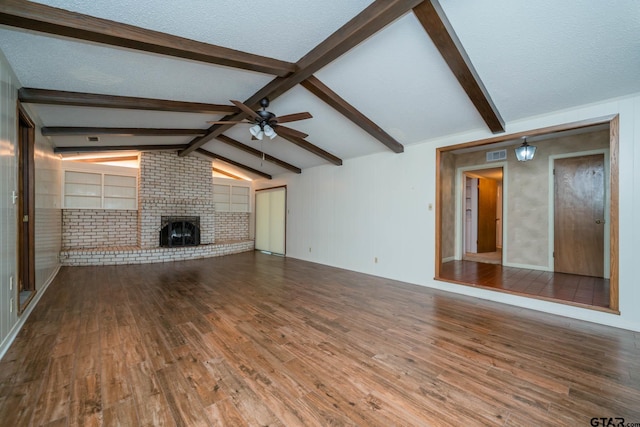 unfurnished living room with a brick fireplace, vaulted ceiling with beams, a ceiling fan, visible vents, and wood finished floors
