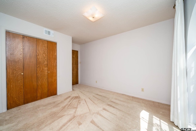 unfurnished bedroom featuring a textured ceiling, visible vents, a closet, and carpet floors