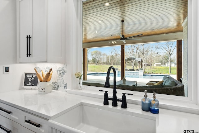 room details featuring white cabinets, ceiling fan, light stone countertops, and sink