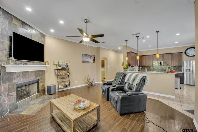 living room featuring ceiling fan, crown molding, and a tile fireplace