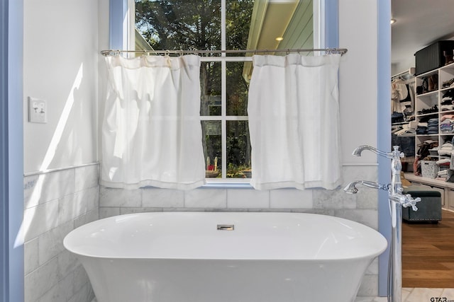 bathroom with hardwood / wood-style flooring, a bathing tub, and tile walls