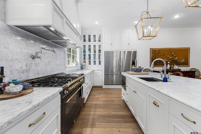 kitchen with sink, appliances with stainless steel finishes, custom range hood, wood-type flooring, and white cabinets