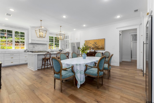 dining area with ornamental molding, light hardwood / wood-style flooring, a notable chandelier, and sink