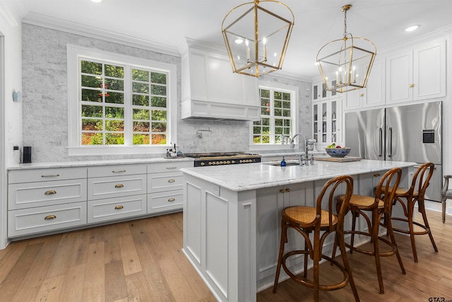 kitchen with stainless steel appliances, light hardwood / wood-style floors, white cabinetry, sink, and a kitchen island with sink