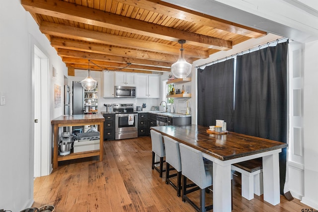 kitchen with stainless steel appliances, hanging light fixtures, beamed ceiling, white cabinetry, and light wood-type flooring